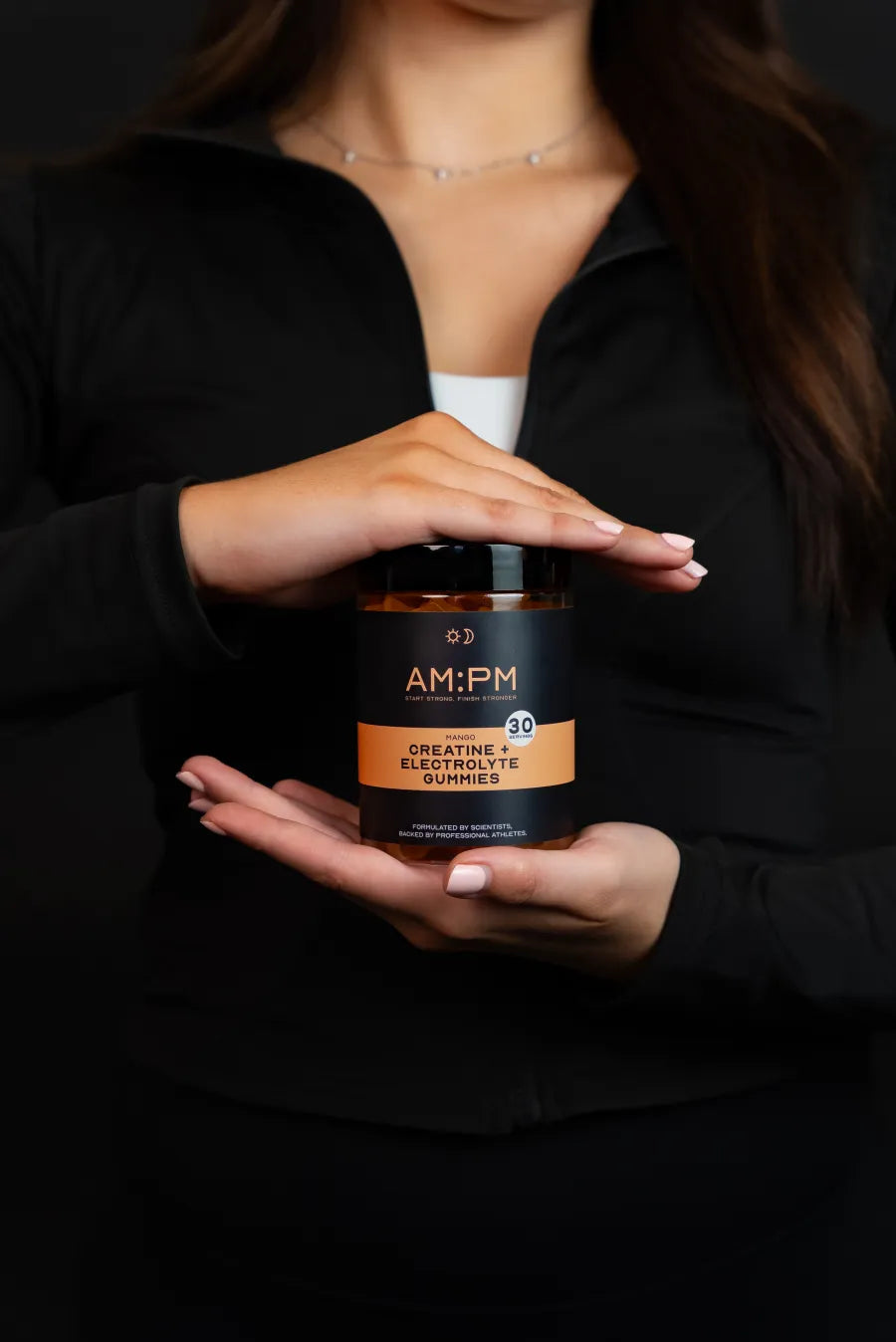 An AM:PM mango creatine and electrolyte gummy tub held between two hands